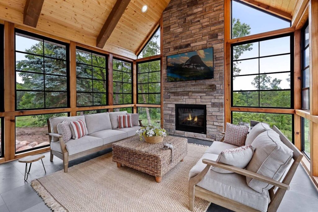 Refined four season room in a Skytop PA home with floor to ceiling windows, exposed timber, and a stone fireplace