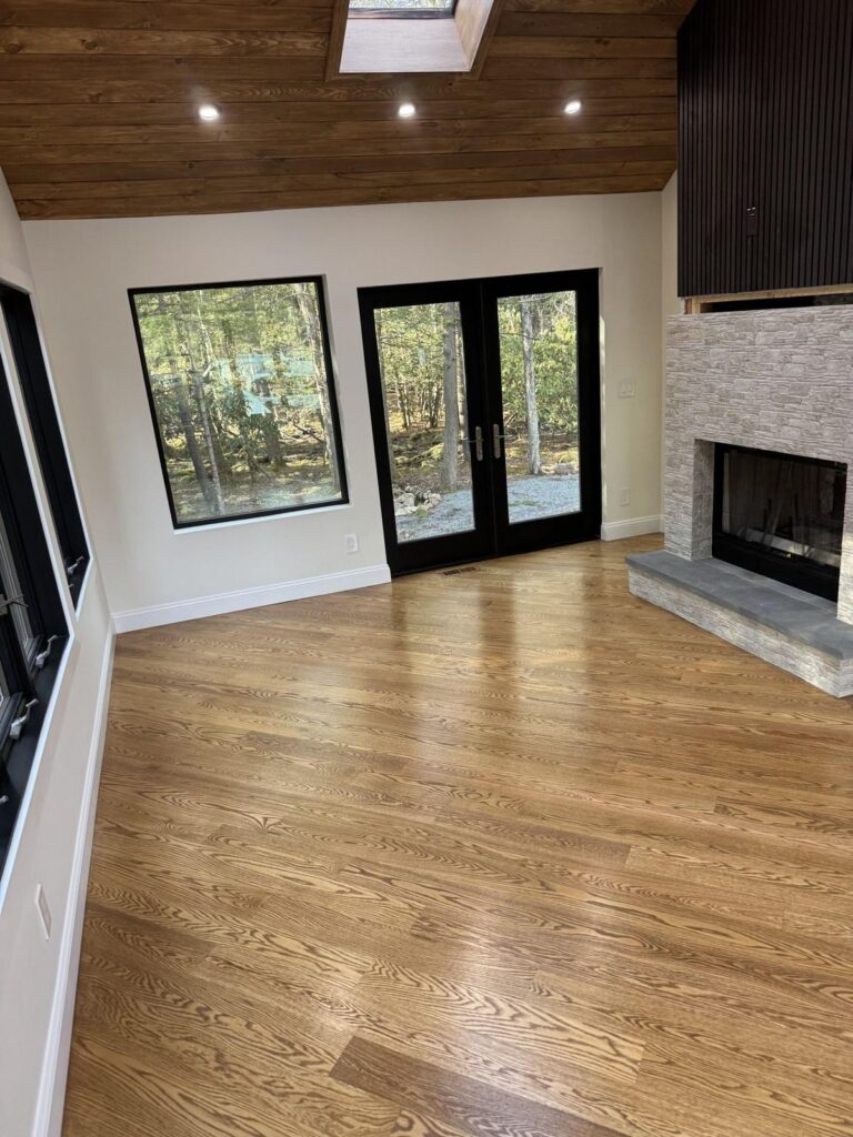 Interior of a Foxtail Builders addition with oversized black windows, wood ceiling, and stone fireplace